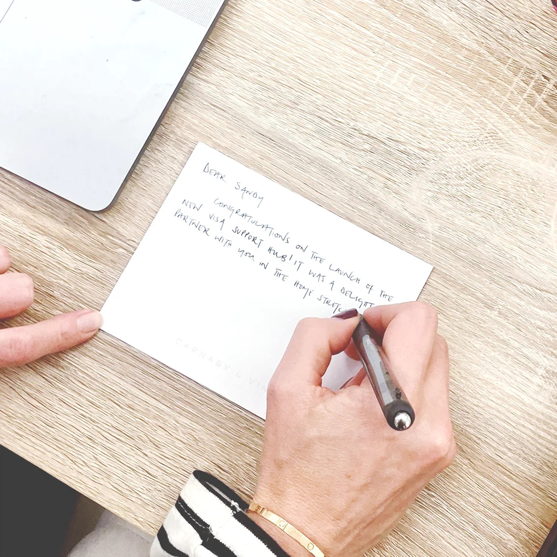 A woman writing a notecard message on a Carnaby & Vine notecard.