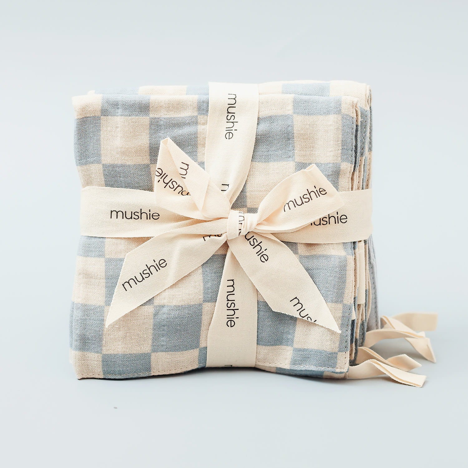 Folded checkered washcloths with a bow and 'mushie' branding on a light gray background