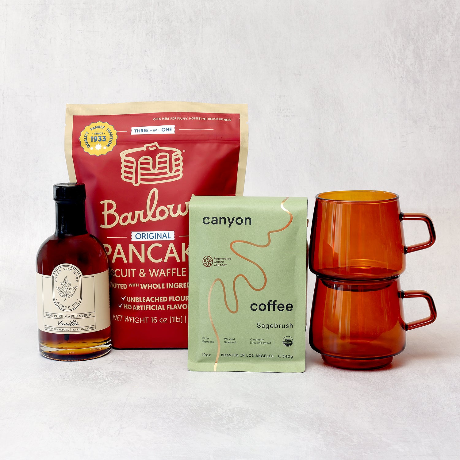 Barlow Pancake Mix, Canyon Coffee, vanilla syrup, and orange mugs on a white background