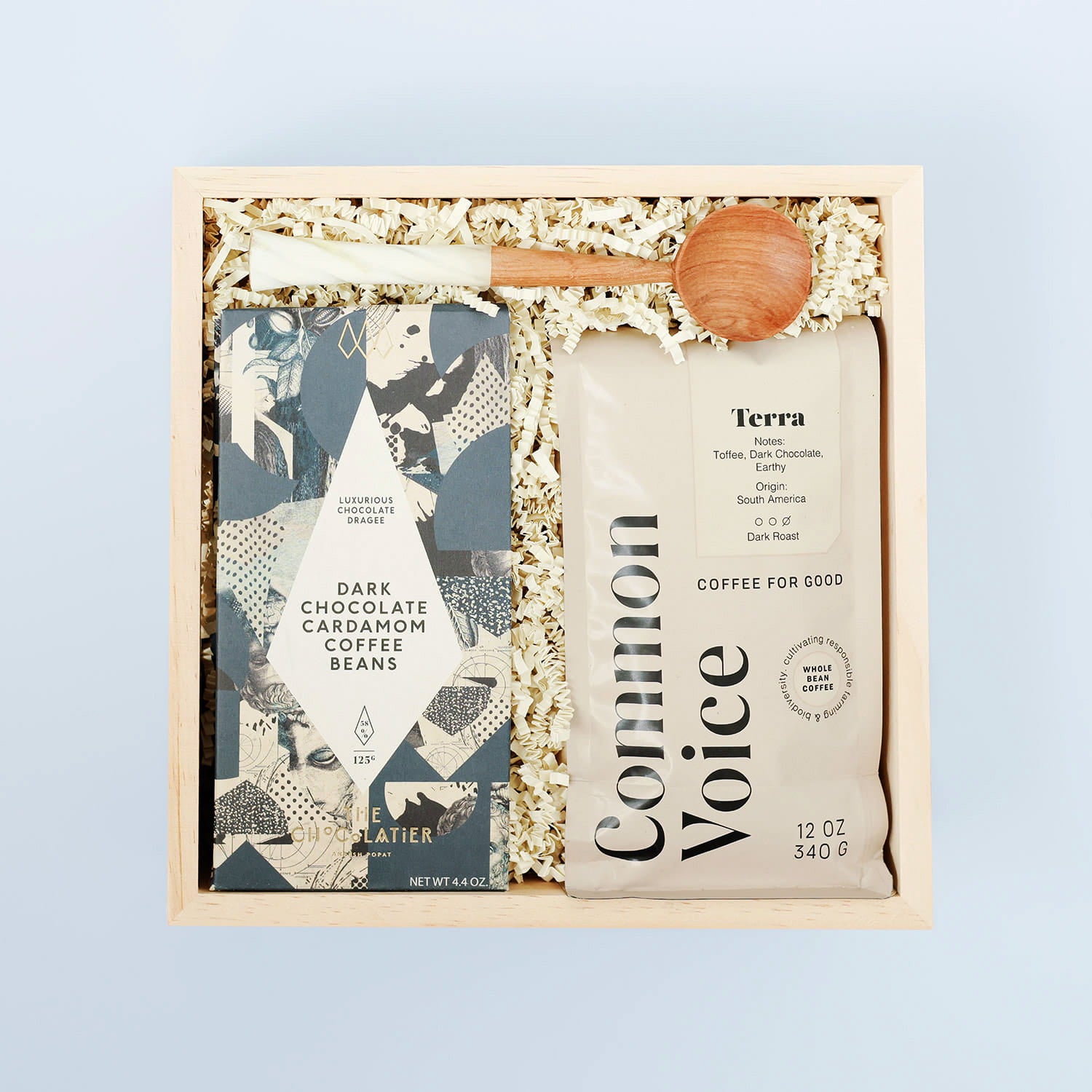 Coffee gift set with coffee beans, chocolate cardamom covered beans, and a wooden spoon on a light blue background