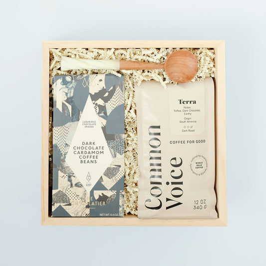 Coffee gift set with coffee beans, chocolate cardamom covered beans, and a wooden spoon on a light blue background