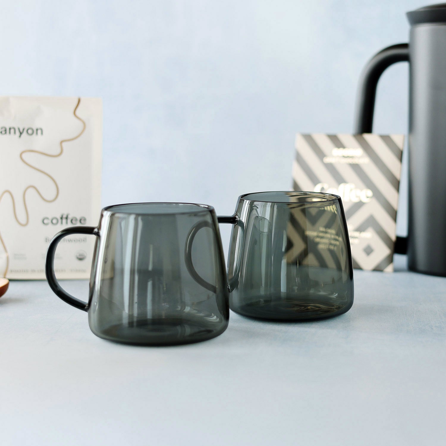 Two dark glass mugs on a light surface with a blurred background
