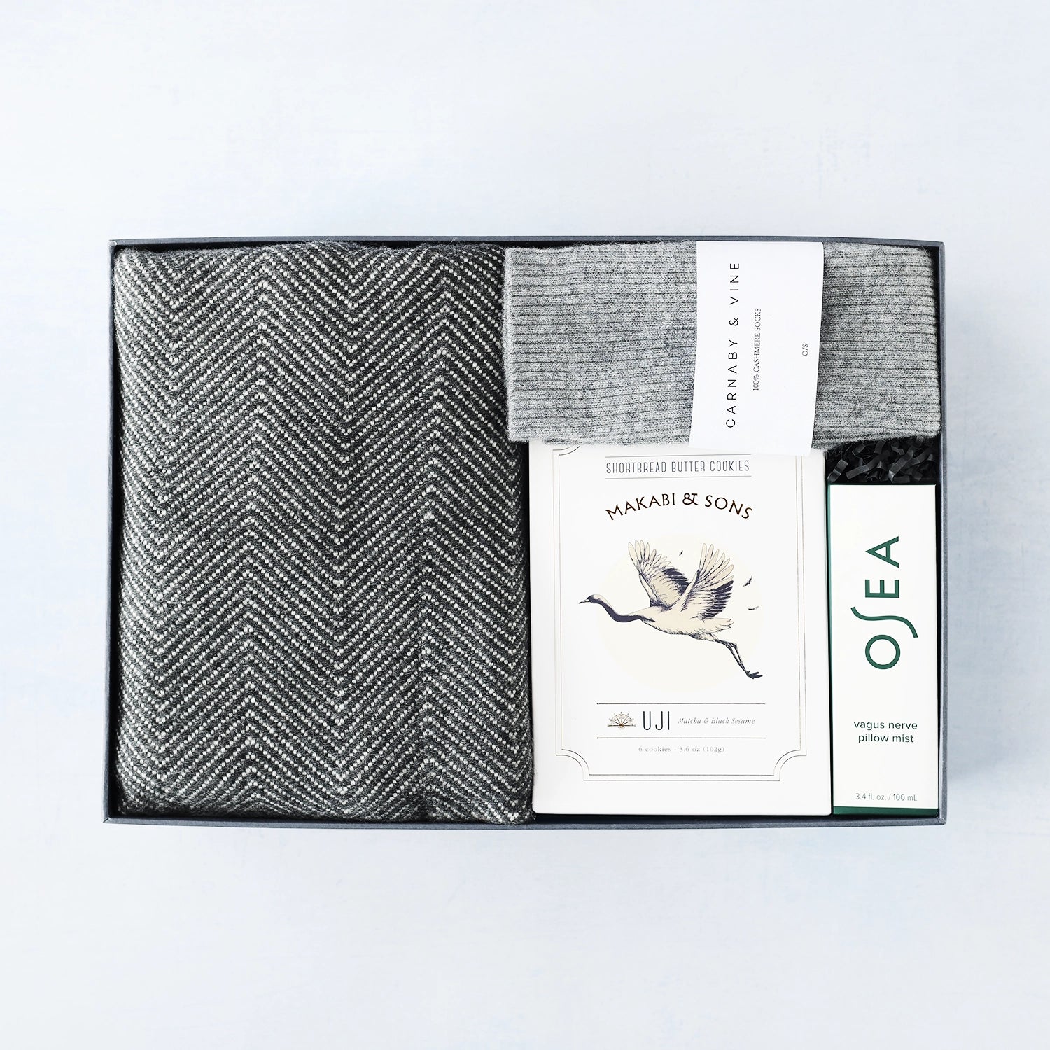 Gray cashmere herringbone blanket in a box with Osea branding on a white background