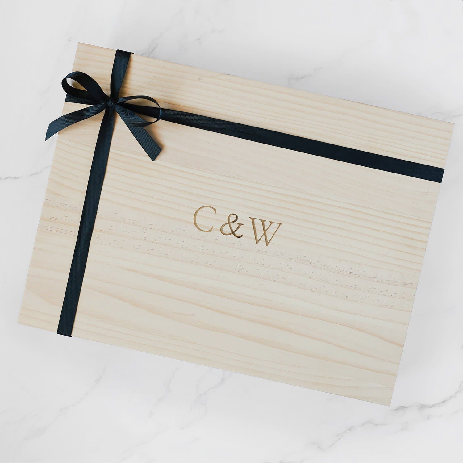 Wooden box with black ribbon and 'C&W' monogram on a white background