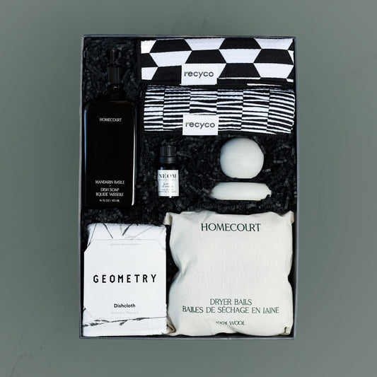 gift box containing eco-friendly cleaning items in black and white tones including homecourt dish soap, recyco towels, neom diffuser oil, concrete passive diffuser, geometry dish towel, homecourt wool dryer balls.
