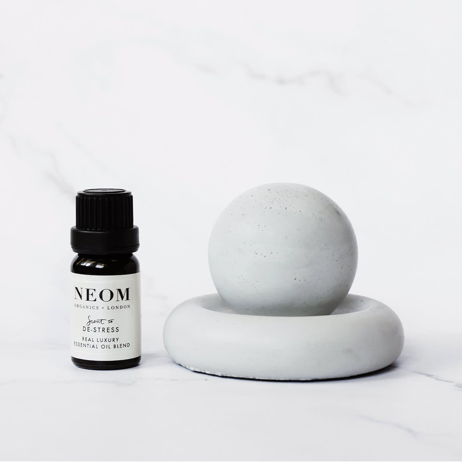 Neom essential oil bottle with a concrete passive diffuser sphere on a light gray background