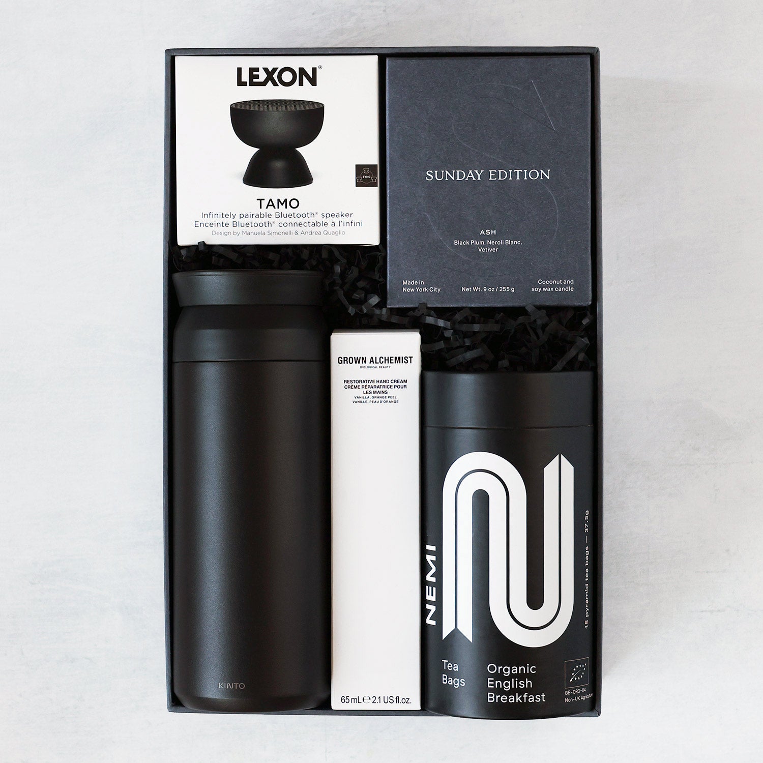 Gift set with black tumbler, Tamo speaker, and candle, hand cream and Nemi tea on a light gray background.