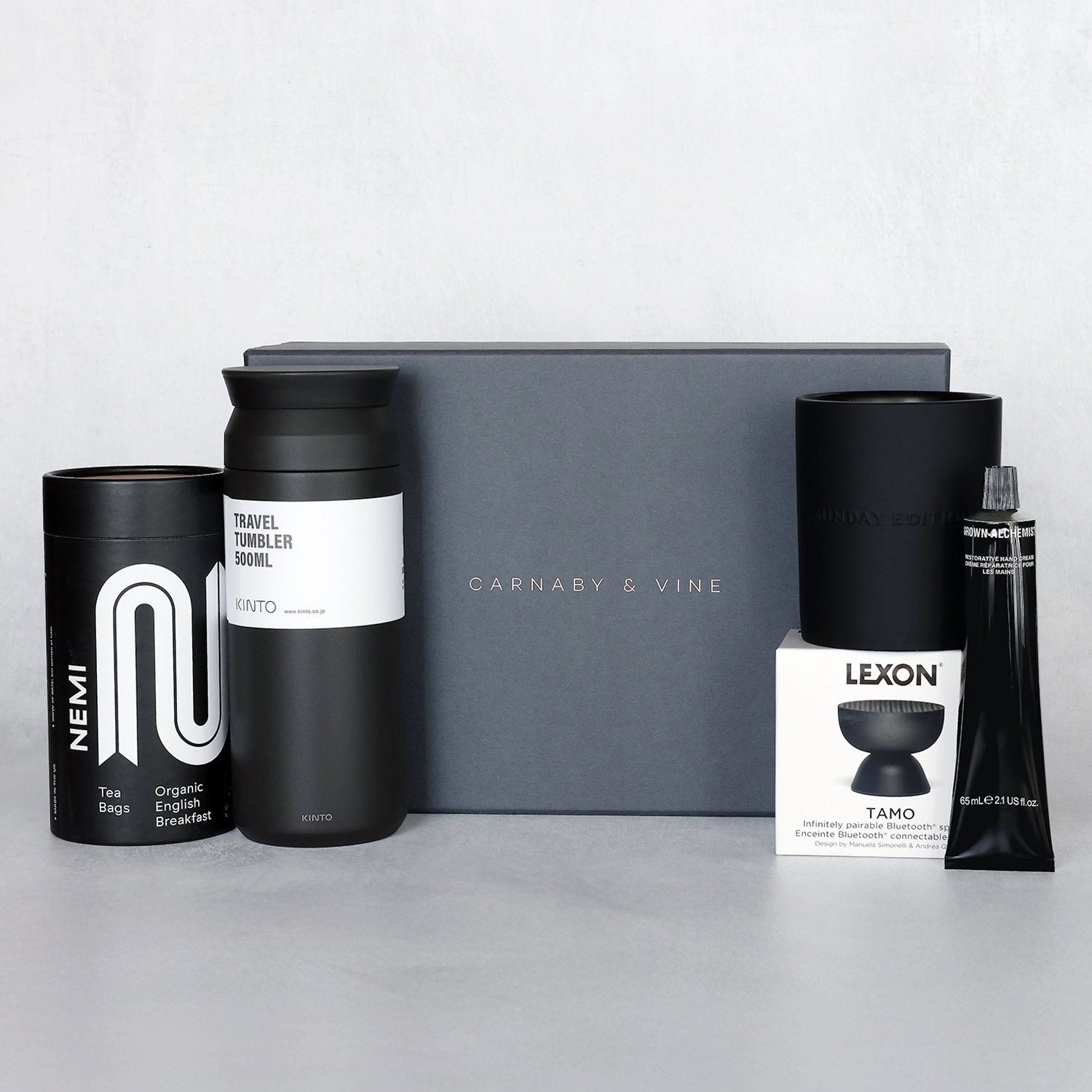 Collection of the black and white products that make up the Elite Retreat gift set including a black Kinto tumbler and black Sunday Edition Ash candle placed in front of a Carnaby & Vine gift box.