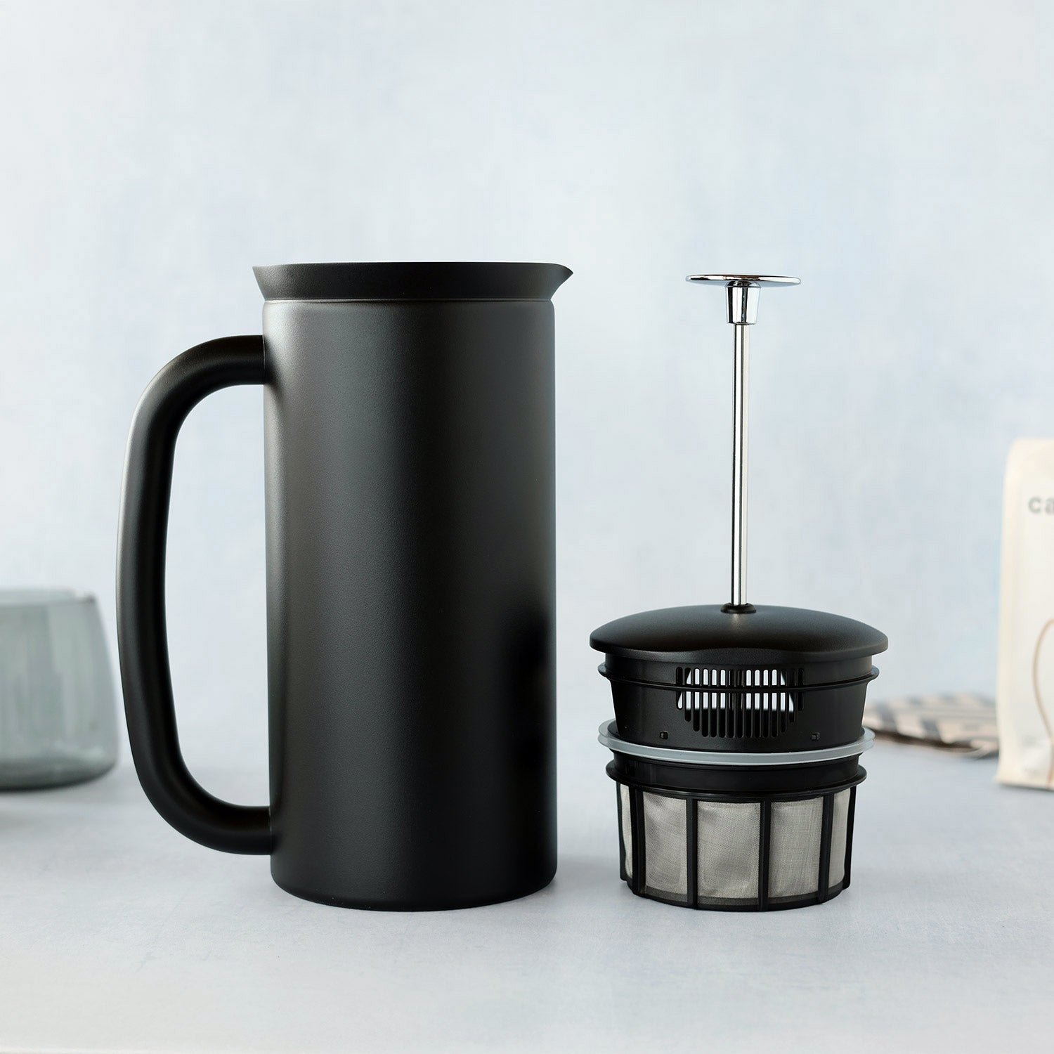 Black coffee press and French press on a light gray blue background.