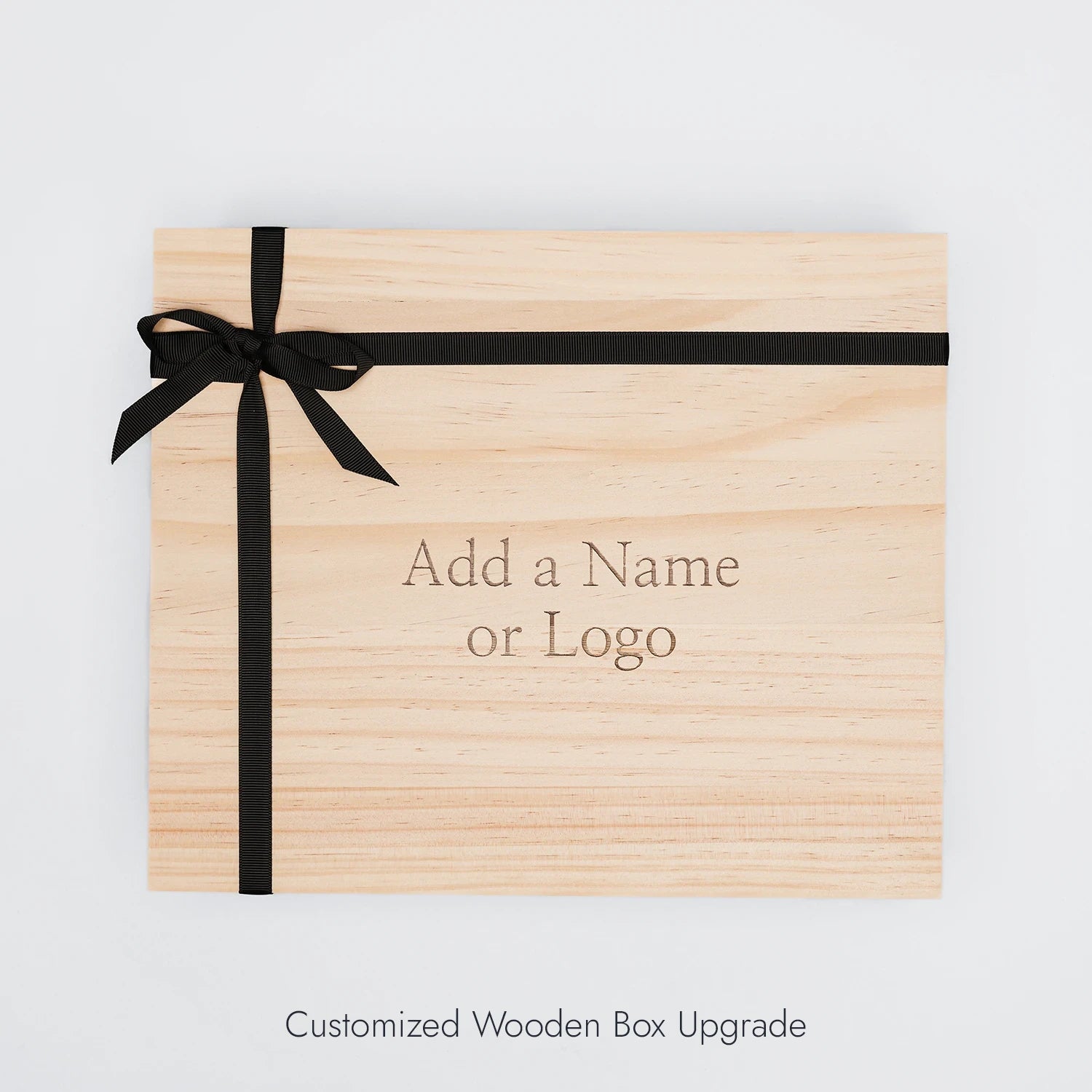 A wooden gift box with a black bow and engraving on the lid.