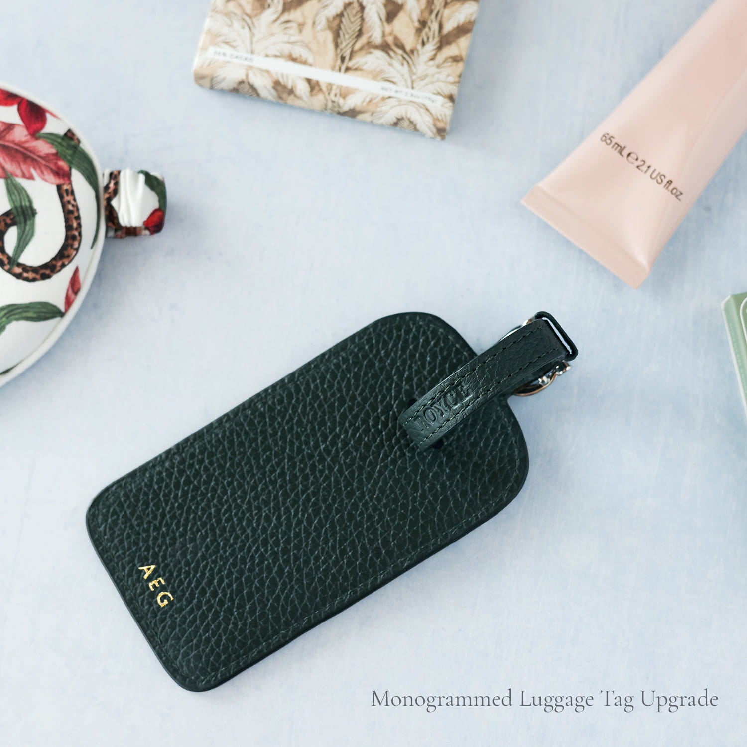 Green monogrammed luggage tag on a light blue surface with travel items.