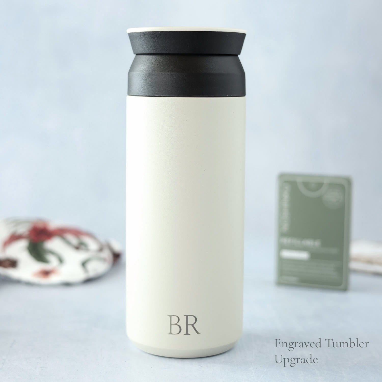 White tumbler with black lid and engraved initials on a light gray background
