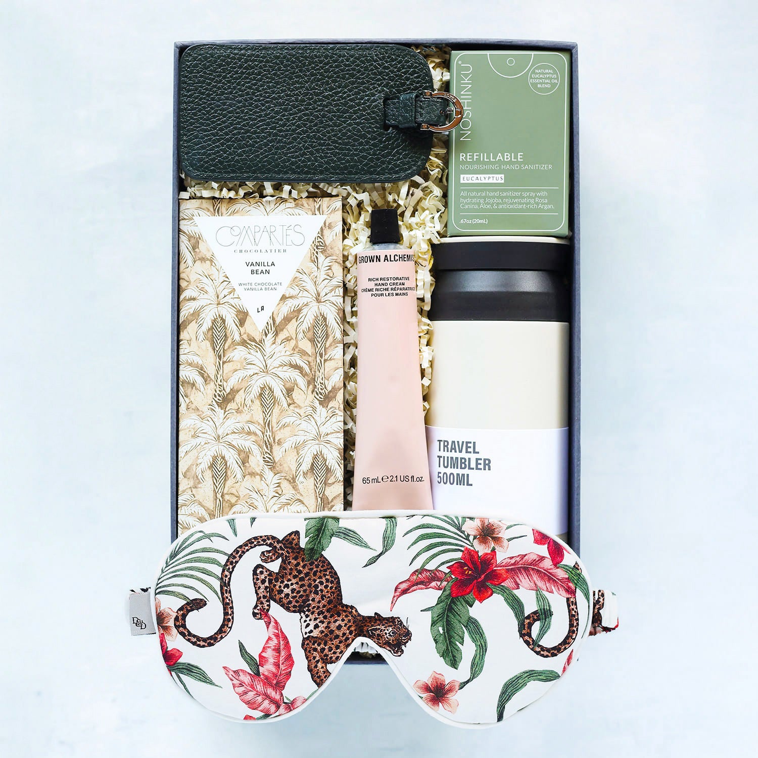 Gift set with travel tumbler, skincare product, and eye mask on a light blue background