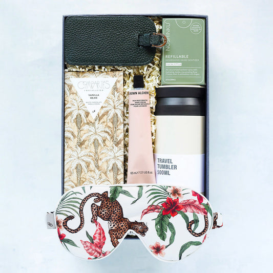 Gift set with travel tumbler, skincare product, and eye mask on a light blue background