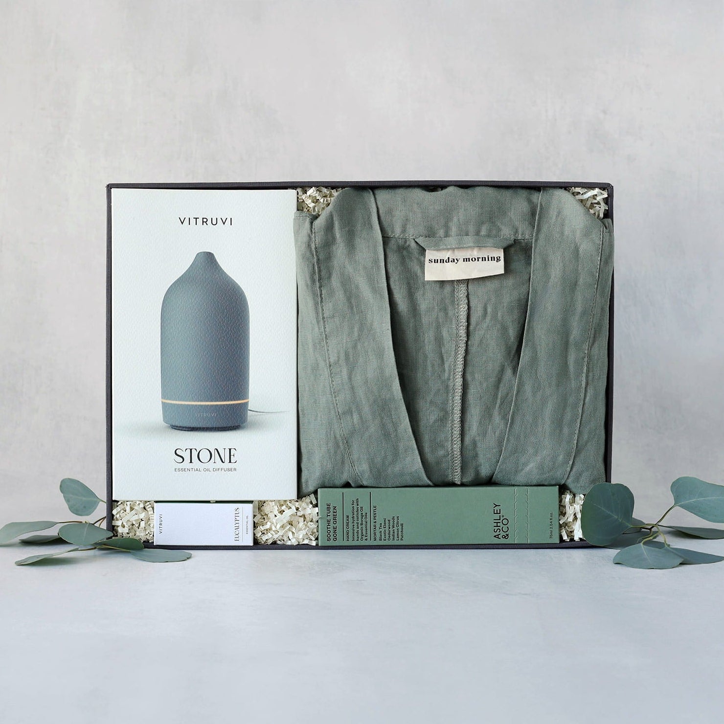 Packaged product with a diffuser and green linen robe on a light gray background